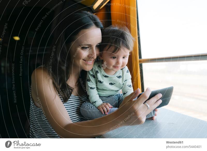 Happy mother and baby girl using smartphone while traveling by train mommy mothers mummy mama mobile phone mobiles mobile phones Cellphone cell phone