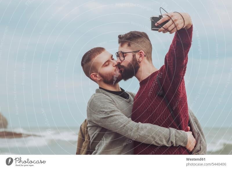 Gay couple taking selfie while kissing in front of the sea Selfie Selfies twosomes partnership couples kisses people persons human being humans human beings