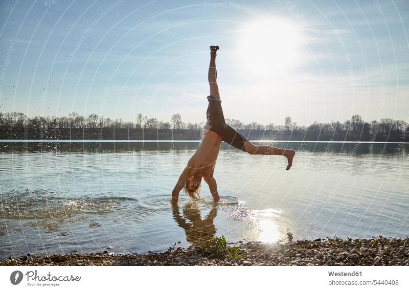 Germany, Bavaria, Feldkirchen, man turning wheels in lake handstand handstands cartwheel doing a cartwheel cartwheeling Parcour lakes men males water waters