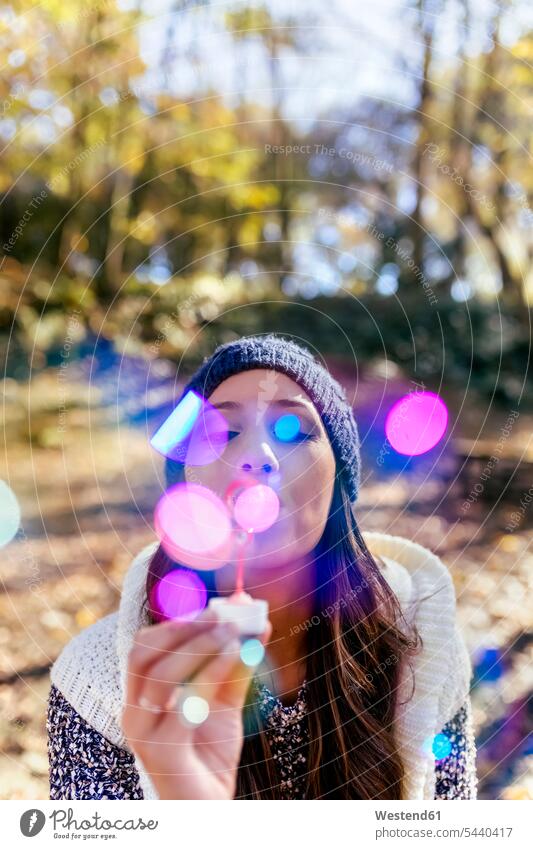 Woman wearing wooly hat blowing soap bubbles in an autumnal forest fall woman females women woolly hat Wooly Hat Knit-Hat Knit Hats wool cap woods forests