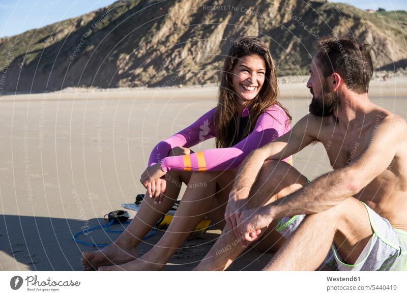 Smiling couple with surfboard sitting on the beach beaches Seated surfboards twosomes partnership couples smiling smile surfer surfers surfing surf ride