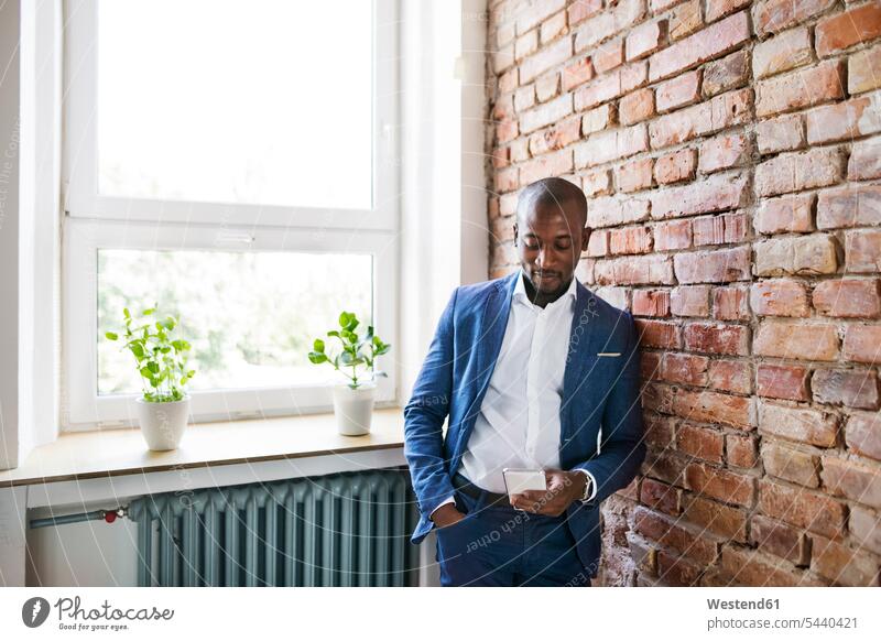 Businessman using cell phone at brick wall by the window mobile phone mobiles mobile phones Cellphone cell phones Business man Businessmen Business men