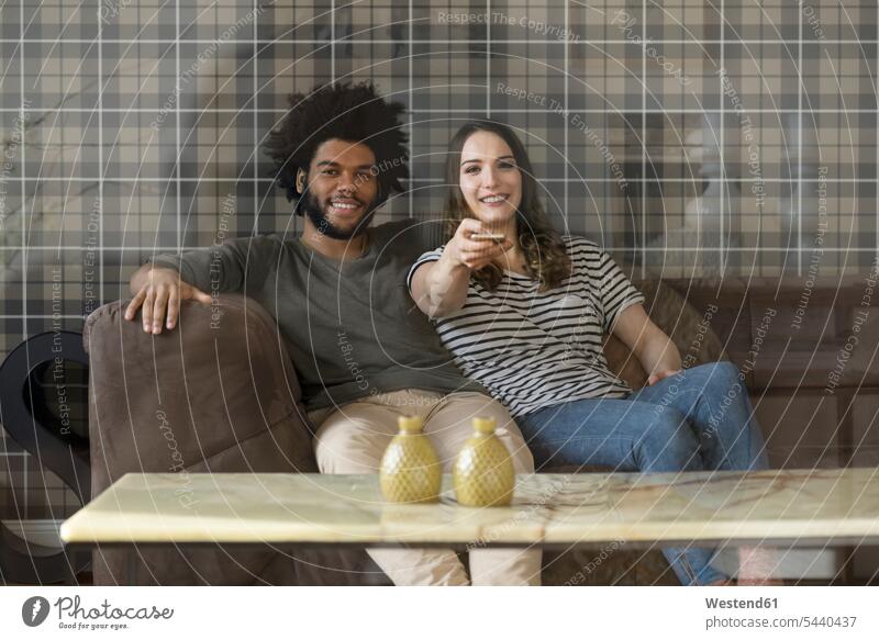 Smiling couple sitting on couch watching Tv settee sofa sofas couches settees twosomes partnership couples smiling smile watching TV Looking At Tv