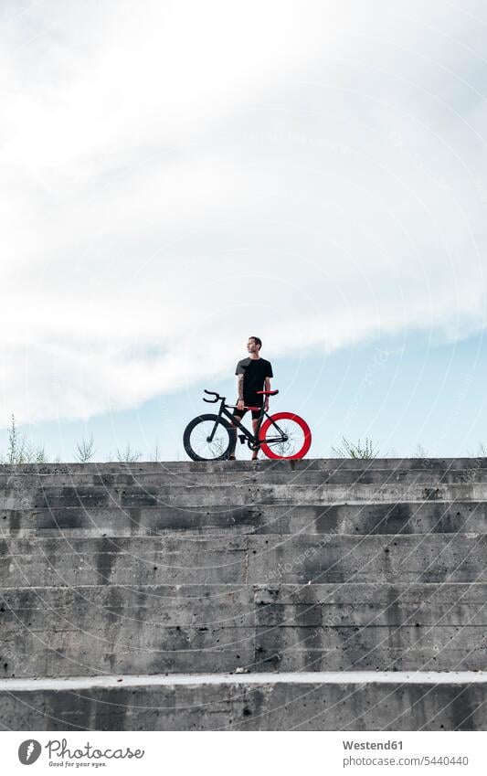 Young man standing with fixie bike on concrete steps men males bicycle bikes bicycles stair Adults grown-ups grownups adult people persons human being humans