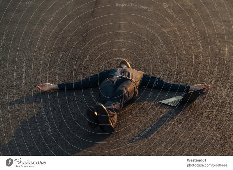 Businessman lying on a road next to laptop laying down lie lying down relax relaxing relaxation business life business world business person businesspeople