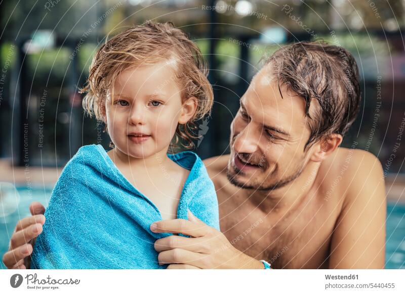 Father toweling daughter at the poolside of an indoor swimming pool swimming bath daughters father pa fathers daddy dads papa drying drying off pool edge