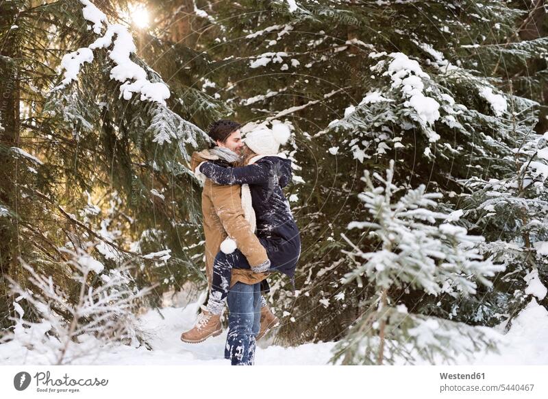 Happy young couple face to face in snow-covered winter forest twosomes partnership couples people persons human being humans human beings Holding Aloft holding