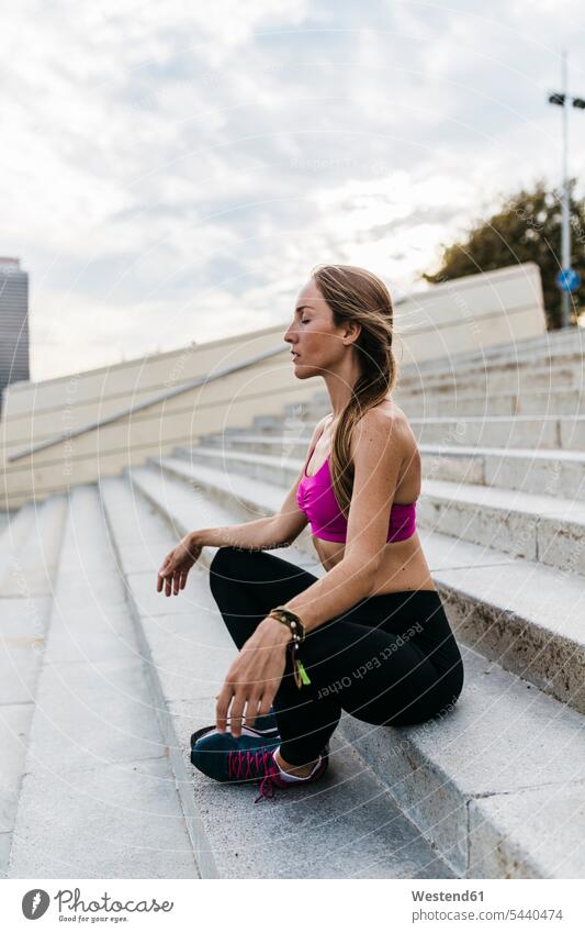 Young woman sitting on stairs after training females women yoga exercising exercise practising Seated warming up warm up Adults grown-ups grownups adult people