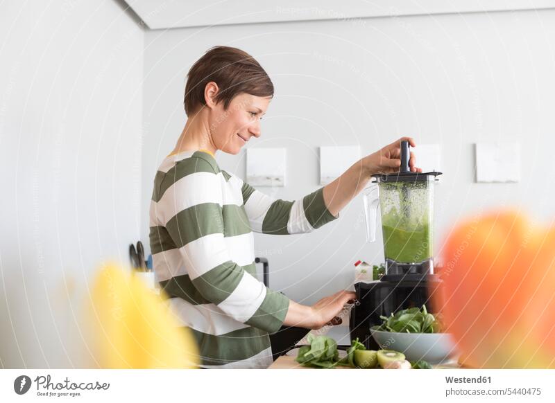Smiling woman preparing green smoothie in the kitchen females women portrait portraits Smoothies Adults grown-ups grownups adult people persons human being