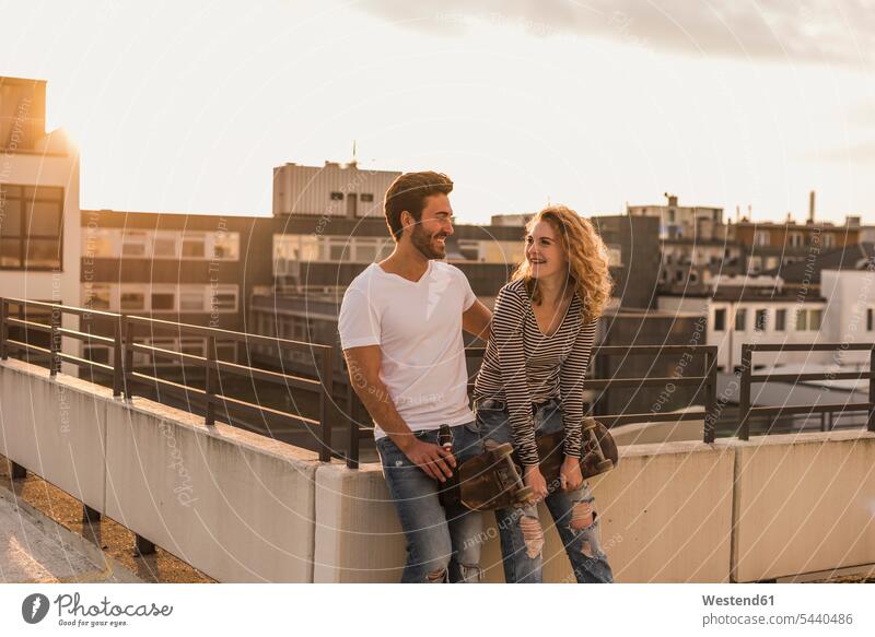 Happy young couple relaxing on roof terrace at sunset deck rooftop sunsets sundown happiness happy twosomes partnership couples relaxation atmosphere