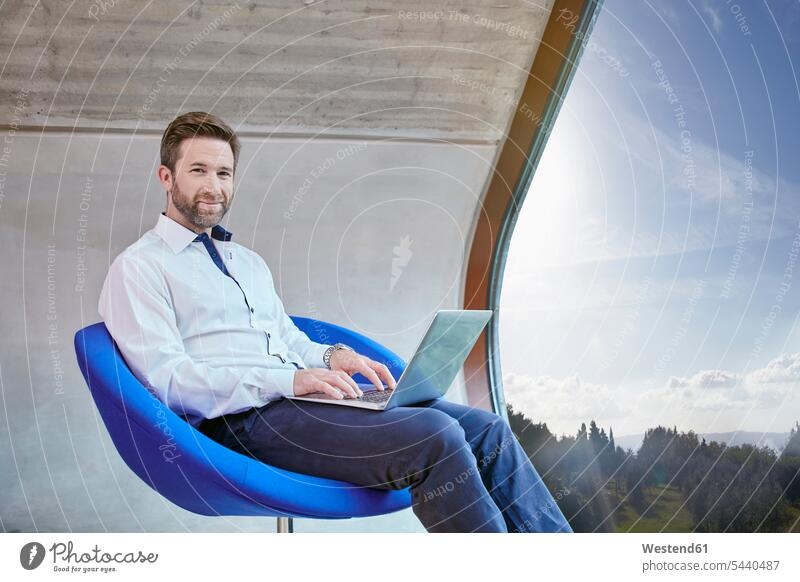 Businessman sitting on chair in attic office using laptop Laptop Computers laptops notebook smiling smile Seated Business man Businessmen Business men computer
