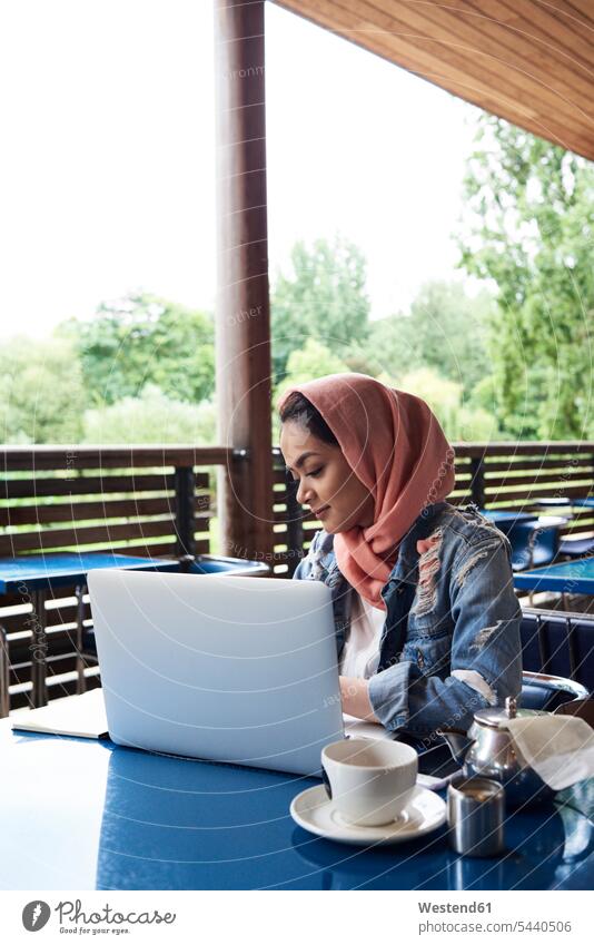 Young woman wearing hijab studying with her laptop on a terrace of a cafe Muslim females women Laptop Computers laptops notebook headscarf head scarf