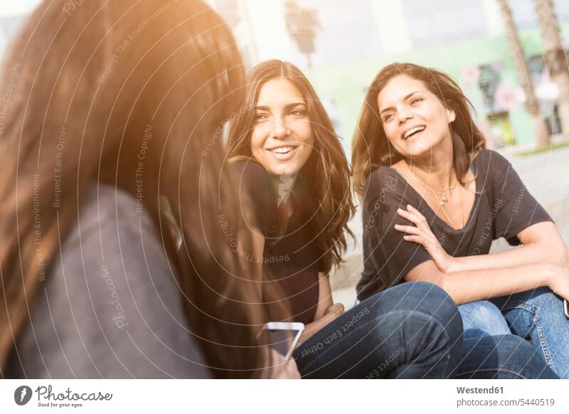 Three happy young women sitting outdoors female friends smiling smile Fun having fun funny mate friendship woman females Seated Adults grown-ups grownups adult