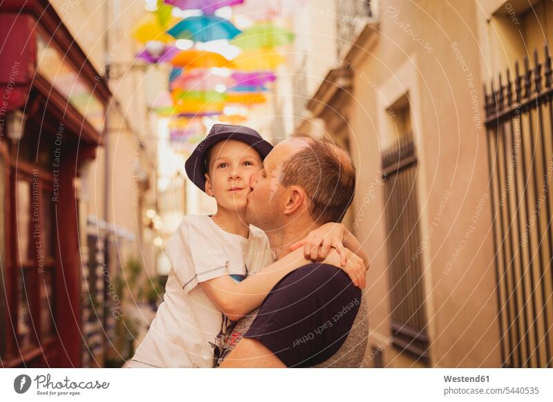 France, Languedoc, Beziers, father kissing son with colorful umbrellas in background kisses pa fathers daddy dads papa sons manchild manchildren parents family
