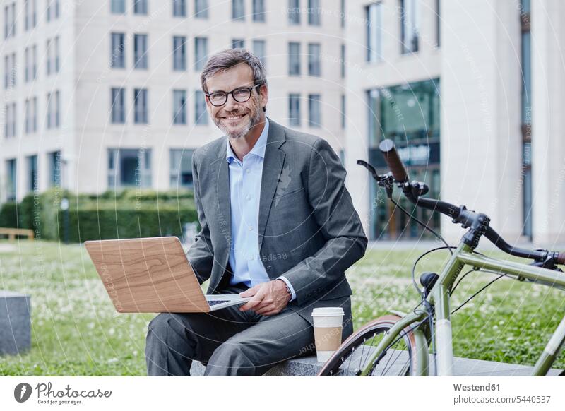 Portrait of smiling mature businessman outdoors with laptop, takeaway coffee and bicycle smile Laptop Computers laptops notebook Businessman Business man