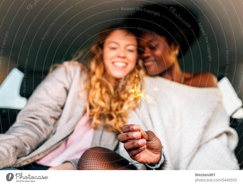 Two best friends sitting in a car playing with sparklers woman females women automobile Auto cars motorcars Automobiles female friends happiness happy Adults