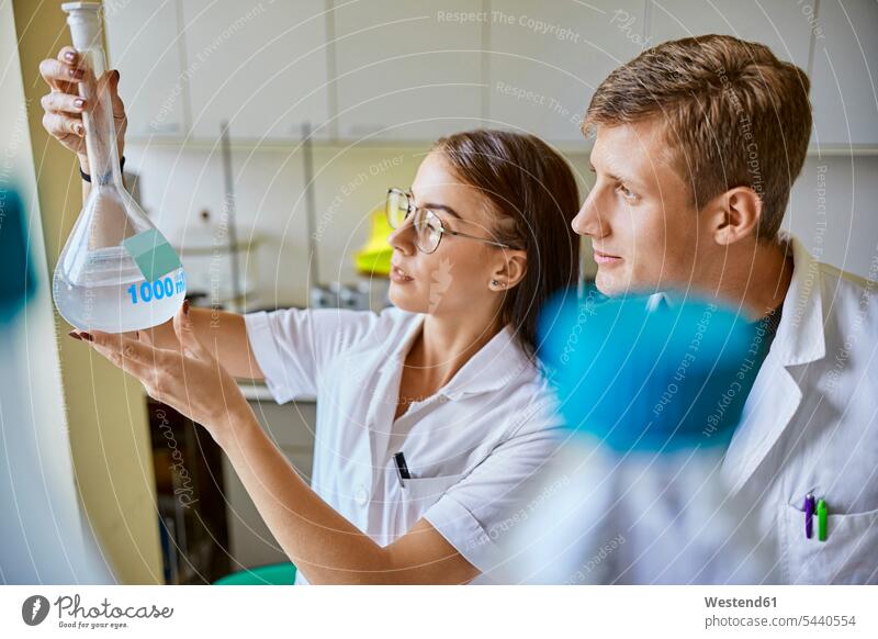 Young man and woman looking at liquid in flask in laboratory eyeing men males recipient Chemical Flasks liquids together females women view seeing viewing