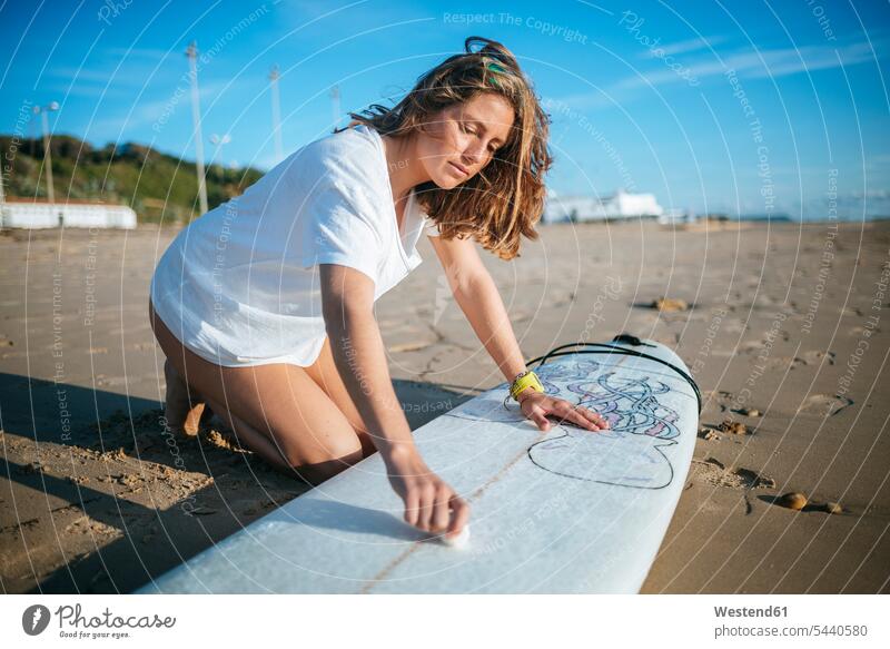Young woman applying paraffin on surfboard on the beach females women surfboards Adults grown-ups grownups adult people persons human being humans human beings