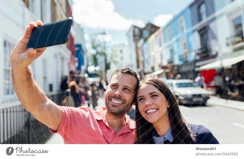 UK, London, Portobello Road, happy couple taking selfie with cell phone twosomes partnership couples Selfie Selfies people persons human being humans