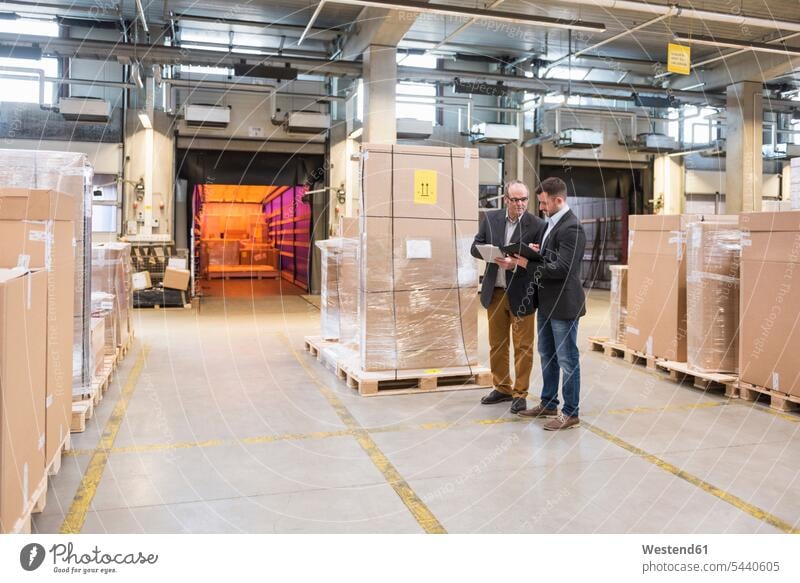 Two men talking in factory warehouse working At Work man males colleagues Businessman Business man Businessmen Business men storehouse storage speaking Adults