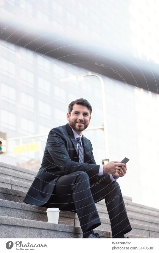 Smiling businessman sitting on stairs with cell phone and takeaway coffee smiling smile break Businessman Business man Businessmen Business men stairway