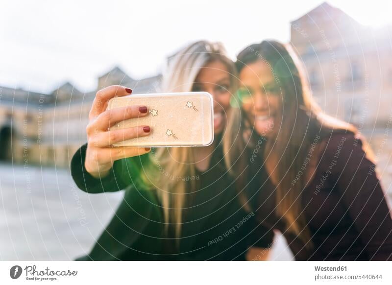 Two playful young women taking a selfie mobile phone mobiles mobile phones Cellphone cell phone cell phones female friends Selfie Selfies woman females mate