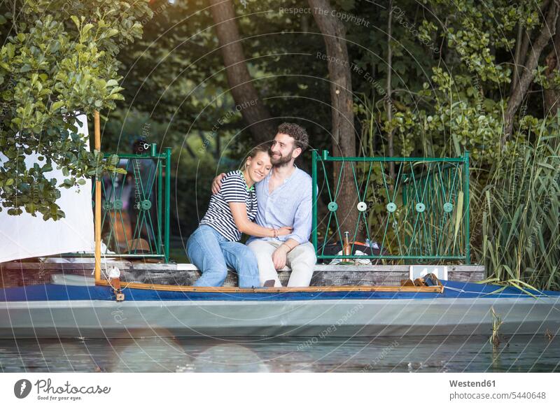 Happy young couple with canoe sitting on a jetty twosomes partnership couples jetties happiness happy Seated canoes boat boats vessel water vehicle people