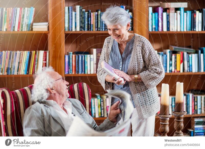 Senior man and woman sitting in library, reading book and newspaper retirement home nursing home senior women elder women elder woman old senior woman armchair