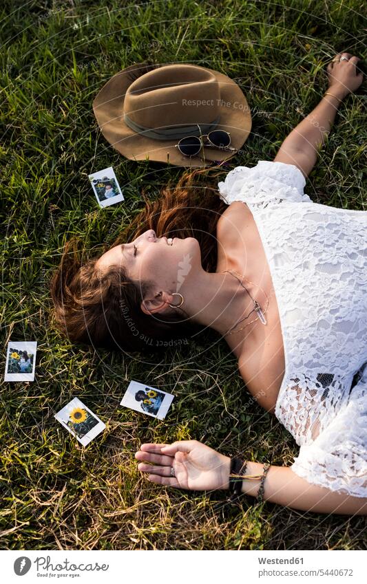 Happy woman lying in a field surrounded by instant photos meadow meadows photograph photographs Field Fields farmland laying down lie lying down females women
