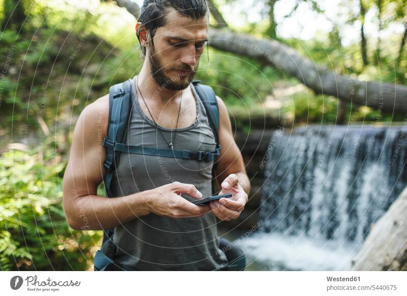 Young man holding cell phone at a waterfall in forest hiking hike mobile phone mobiles mobile phones Cellphone cell phones men males hiker wanderers hikers