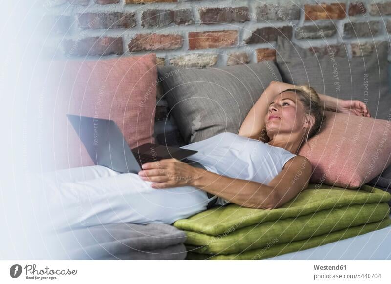 Mature woman lying on couch, usine laptop home at home country house country houses cottage cottages Country Cottage Laptop Computers laptops notebook