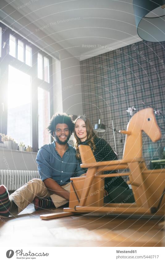 Smiling couple looking at camera in front of rocking horse twosomes partnership couples rocking horses home at home smiling smile people persons human being