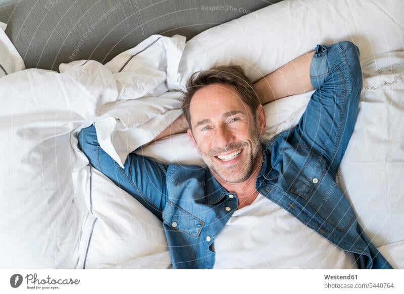 Portrait of happy mature man lying on bed with hands behind head men males beds portrait portraits Adults grown-ups grownups adult people persons human being
