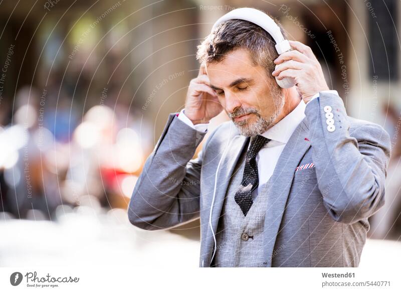 Mature businessman with headphones in the city hearing men males headset town cities towns Adults grown-ups grownups adult people persons human being humans