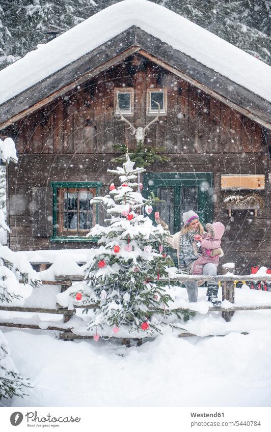 Austria, Altenmarkt-Zauchensee, mother with little son decorating Christmas tree at wooden house snow winter hibernal family families mommy mothers mummy mama