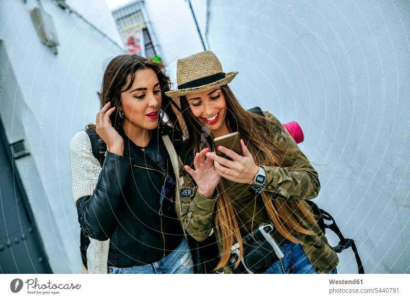 Two young women in a town looking at cell phone female friends mobile phone mobiles mobile phones Cellphone cell phones smiling smile mate friendship telephones