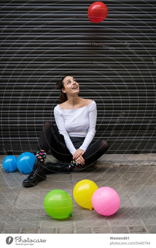 Young woman sitting on pavement watching flying balloon balloons females women Adults grown-ups grownups adult people persons human being humans human beings