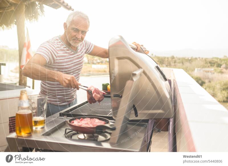 Mature man grilling steaks on a gas grill on his penthouse terrace barbecueing Barbecuing men males Steak Steaks smiling smile Adults grown-ups grownups adult