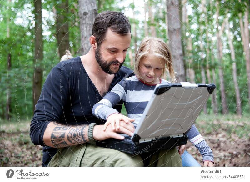 Father and daughter in forest using laptop daughters man men males woods forests Laptop Computers laptops notebook girl females girls father pa fathers daddy