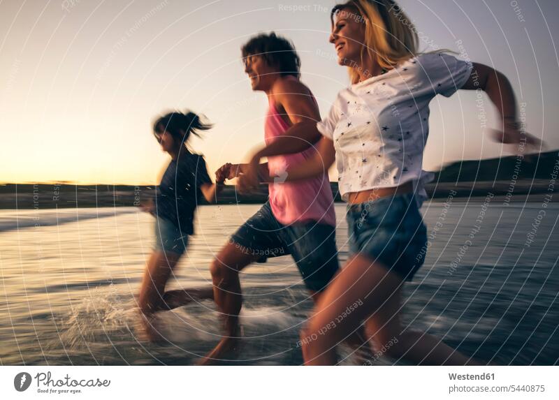 Happy friends holding hands and running into the sea at dusk ocean Fun having fun funny happiness happy water waters body of water friendship vacation Holidays