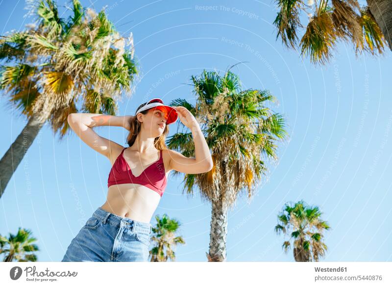 Portrait of young woman with bikini and sun visor with blue sky background and palm trees standing females women Adults grown-ups grownups adult people persons