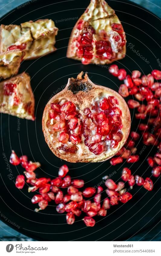 Half of pomegranate and pomegranate seed on black plate, close-up nobody sliced Preparation prepare preparing peeled preparation Freshness fresh healthy eating