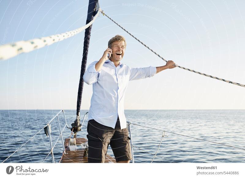 Laughing mature man on the phone on his sailing boat men males boat sports Adults grown-ups grownups adult people persons human being humans human beings