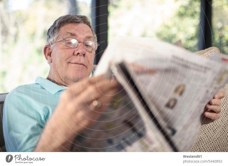 Senior man sitting on couch reading newspaper men males newspapers Seated settee sofa sofas couches settees home at home senior men senior man elder man