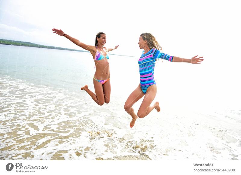 Two women having fun on the beach female friends jumping Leaping beaches Fun funny woman females mate friendship jumps Adults grown-ups grownups adult people