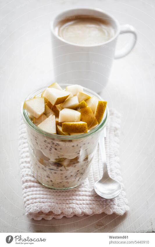 Glass of overnight oats with chia seeds, almond milk and pears tea spoon Teaspoon tea spoons black chia seeds sliced Coffee Cup Coffee Cups garnished prepared
