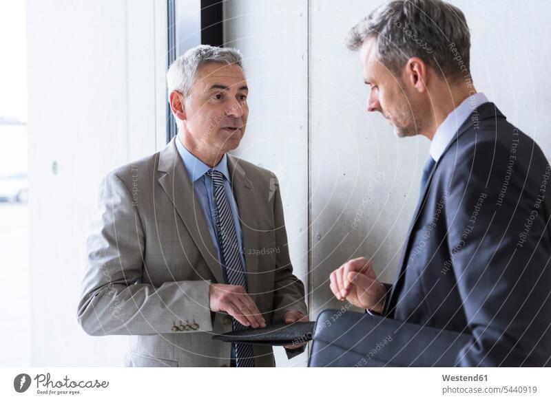 Two businessmen having an informal meeting office offices office room office rooms standing discussing expertise competence competent work meeting briefing