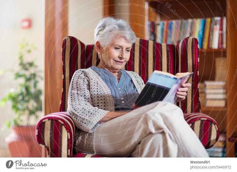 Senior woman siting in library, reading book sitting Seated armchair Arm Chairs armchairs retirement home nursing home books senior women elder women