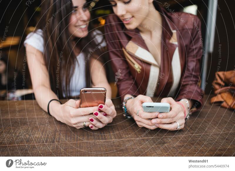 Two young women using cell phones in a bar smiling smile female friends mobile phone mobiles mobile phones Cellphone mate friendship telephones communication