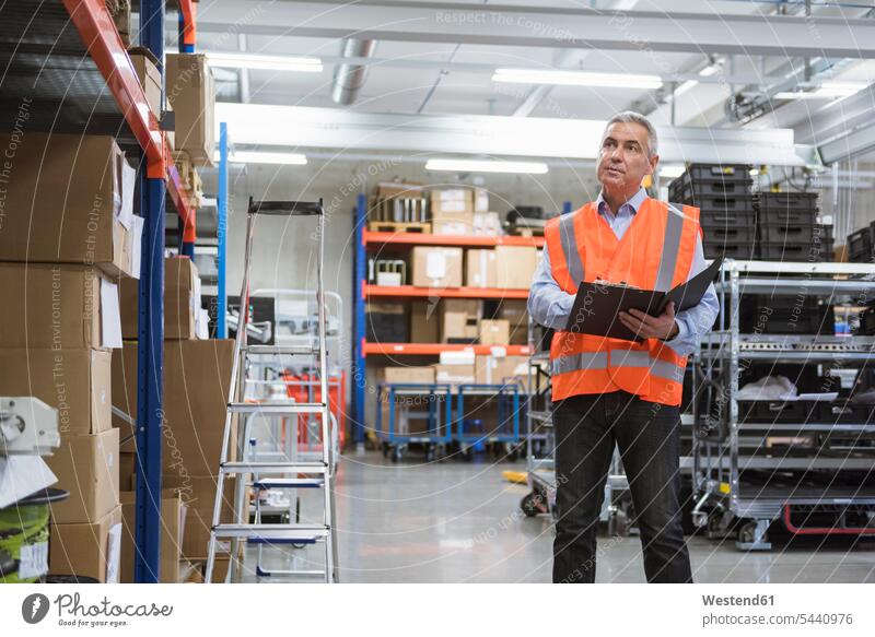 Man in factory hall wearing safety vest holding clipboard man men males working At Work scrutiny scrutinizing clipboards clip-board clip-boards clip board